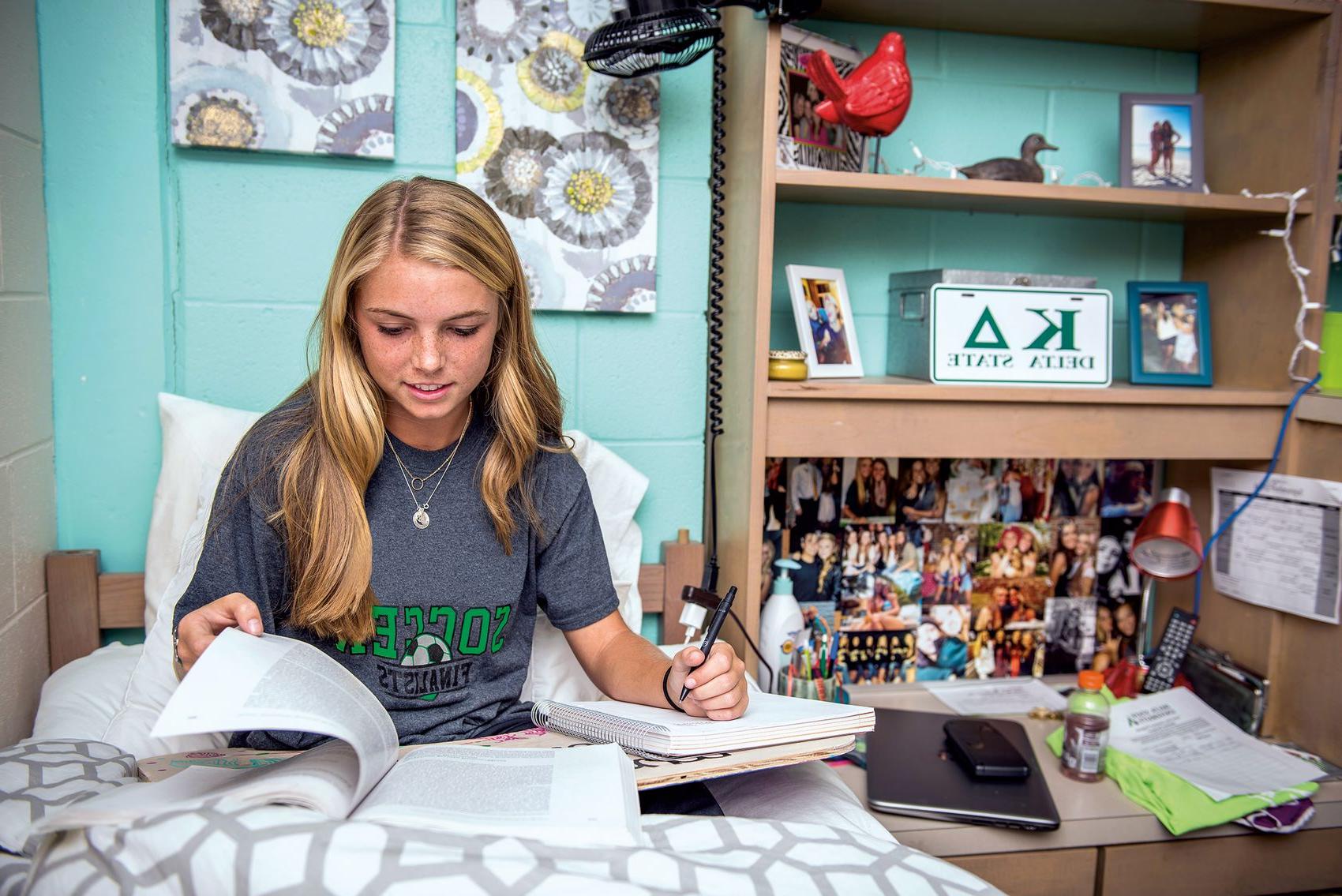 A girl studies in bed in a decorated Delta State freshman residence hall room.